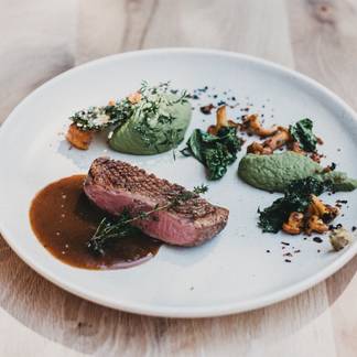 Rosa gebratenes Fleisch mit kräftiger Sauce, grünen Gemüsecremes, Blattgemüse und Pilzen, fein angerichtet.