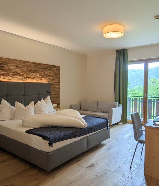 Zimmer Molzbach mit Doppelbett, Schreibtisch, Sofa und Balkon im Naturhotel Molzbachhof.