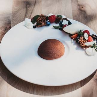 Schokoladendessert in Halbkugelform mit frischen Beeren, Creme und knusprigen Elementen.